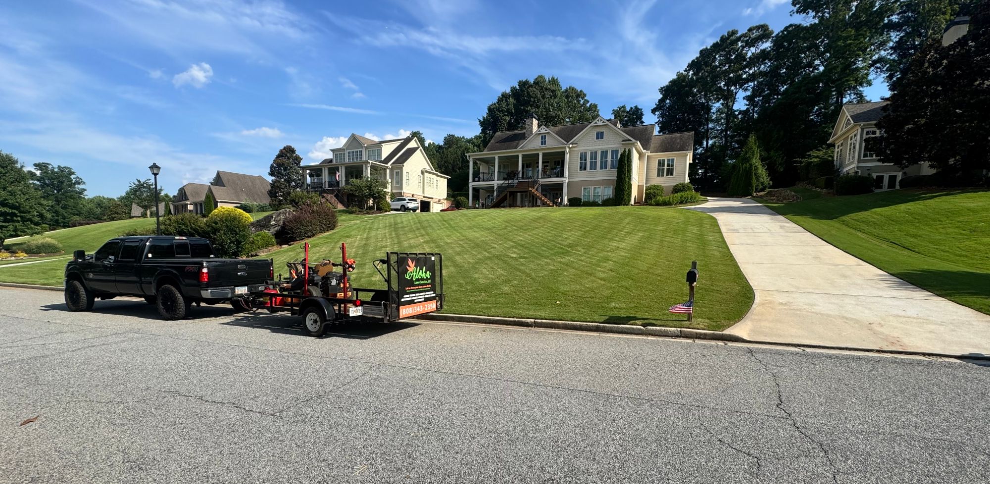 Aloha Lawn Services truck and equipment trailer parked beside a freshly mowed lawn in Newnan, Georgia